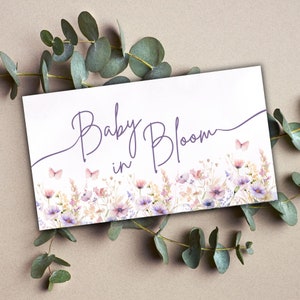 May include: A white card with purple text that reads "Baby in Bloom" and a floral design with butterflies. The flowers are in shades of pink, purple, and yellow.