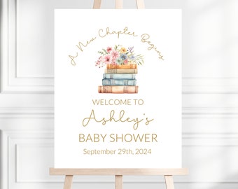 May include: A white welcome sign with gold text that reads "A New Chapter Begins" with a stack of books and flowers on top. The text also reads "Welcome to Ashley's Baby Shower September 29th, 2024".