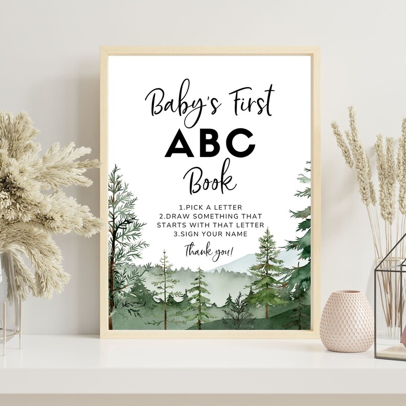 Może przedstawiać: Drukowana tablica z akwarelowym tłem lasu z zielonymi drzewami. Tablica zawiera napis "Baby's First ABC Book" i instrukcje do gry na baby shower: "1. Wybierz literę, 2. Narysuj coś, co zaczyna się od tej litery, 3. Podpisz się. Dziękuję!"