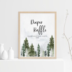 May include: A rectangular sign in a light wood frame featuring a watercolour forest of green pine trees at the bottom. The text reads Diaper Raffle and below it, PLEASE LEAVE YOUR TICKETS HERE in black lettering against a white background.