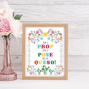 Può includere: Un cartello stampabile con sfondo bianco e bordo floreale colorato. Il testo dice "Grab a Prop Strike a Pose and Say Queso!"