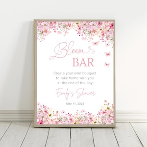 May include: A pink and white floral sign with the text "Bloom Bar" and the message "Create your own bouquet to take home with you at the end of the day!"  The sign also includes the text "Emily's Shower" and the date "May 11, 2025".