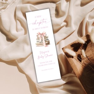 May include: A white bookmark with pink text and illustrations. The text reads "A New Chapter is About to Begin" and "Megan's Baby Shower." A stack of books with a pink bow is also featured.