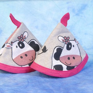 Puede incluir: Dos agarraderas de olla en forma de cono, con un diseño de vaca rosa y blanca y un borde rosa.