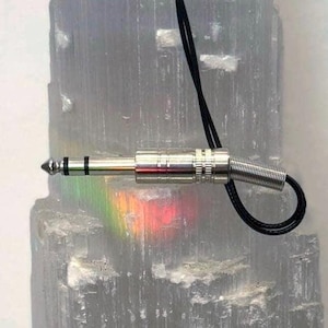 May include: A silver-colored audio jack with a black cord loop. The jack is set against a background of a translucent, crystalline structure, with a rainbow spectrum of light visible.