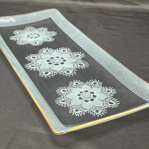 Puede incluir: Una bandeja rectangular de servir de vidrio con un borde dorado y tres diseños de encaje grabados.