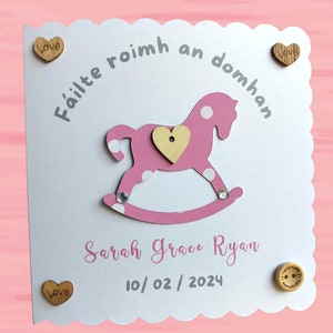 Biglietto per bebè personalizzato per bambina con disegno rosa di cavallo a dondolo in lingua irlandese per nuovi genitori orgogliosi