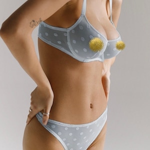 Pode incluir: Conjunto de lingerie azul claro com bolinhas brancas. O sutiã e a cueca a condizer apresentam um design delicado. O sutiã tem alças ajustáveis e aros. O conjunto é feito de um tecido macio e transparente.