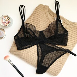 Black lace lingerie set with a scalloped design. The bra has adjustable straps and a hook and eye closure. The panty has a low rise and a thong back.