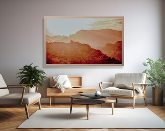 May include: A framed photograph of a mountain range at sunset. The mountains are a warm orange color, and the sky is a light blue with a few clouds. The photograph is in a light wood frame.