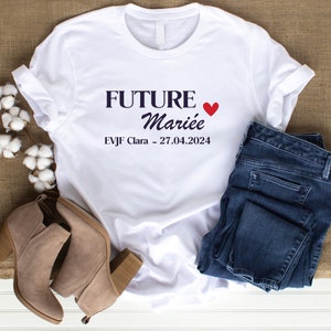 Peut inclure: T-shirt blanc avec le texte "FUTURE Mariée" en noir avec un cœur rouge. Le texte "EVJF Clara - 27.04.2024" est également imprimé en noir.