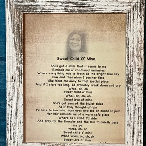 May include: A framed print with a vintage aesthetic featuring a poem titled "Sweet Child O' Mine". The poem is written in a cursive font and describes a person with a smile that reminds the author of childhood memories. The poem also mentions blue skies, rain, and a warm safe place.