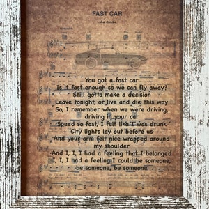 May include: A vintage-style print of sheet music with lyrics to the song "Fast Car" by Luke Combs. The lyrics are printed on a brown background with a black car silhouette in the background.