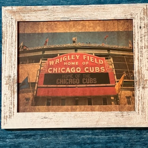 May include: A vintage-style print of Wrigley Field, home of the Chicago Cubs. The red and white sign reads "Wrigley Field, Home of the Chicago Cubs".