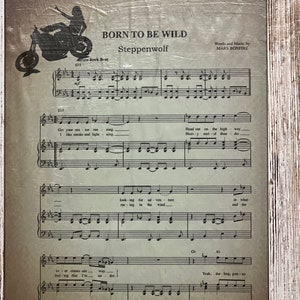 May include: Framed print of sheet music for "Born to Be Wild" by Steppenwolf. The image features a motorcycle silhouette and musical notation. The frame is white with a distressed, rustic finish.