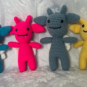 May include: Four handmade crochet monster dolls in shades of blue, pink, gray, and yellow. Each doll has large ears, small wings, and a smiling face. The dolls are approximately 6 inches tall.