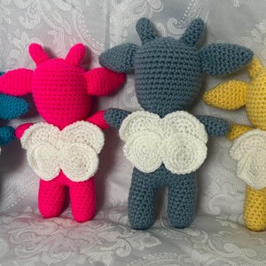 Puede incluir: Cuatro mu&ntilde;ecos de ganchillo hechos a mano en azul, rosa, gris y amarillo. Cada mu&ntilde;eco tiene un pecho blanco en forma de nube y orejas peque&ntilde;as. Los mu&ntilde;ecos est&aacute;n de pie, mostrando sus variaciones de color &uacute;nicas y detalles hechos a mano.