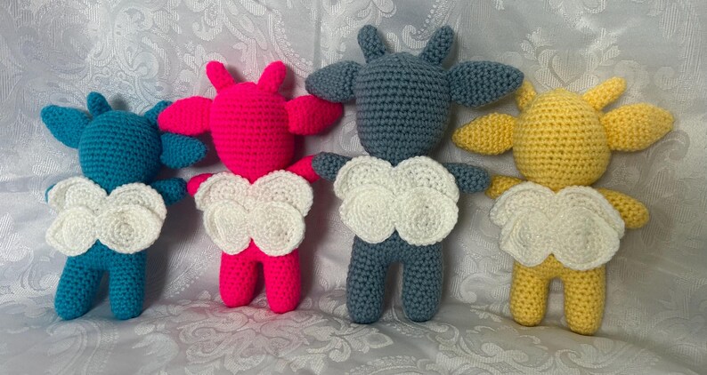 Puede incluir: Cuatro mu&ntilde;ecos de ganchillo hechos a mano en azul, rosa, gris y amarillo. Cada mu&ntilde;eco tiene un pecho blanco en forma de nube y orejas peque&ntilde;as. Los mu&ntilde;ecos est&aacute;n de pie, mostrando sus variaciones de color &uacute;nicas y detalles hechos a mano.