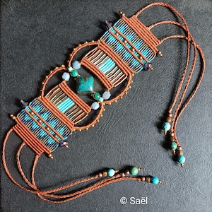 Pode incluir: Colar de macramé feito à mão com contas turquesas e azuis, e uma pedra quadrada turquesa. O colar tem um cordão castanho e um design intrincado tecido. O design inclui pequenas contas douradas e uma pedra quadrada turquesa.