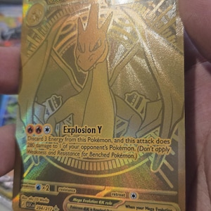 Puede incluir: Una carta coleccionable dorada que muestra a Mega Charizard Y con 360 HP. La carta presenta el texto Explosion Y, que descarta 3 Energ&iacute;as y causa 280 de da&ntilde;o. Incluye la regla Mega Evolution ex y el n&uacute;mero de serie 294/217 en la parte inferior.