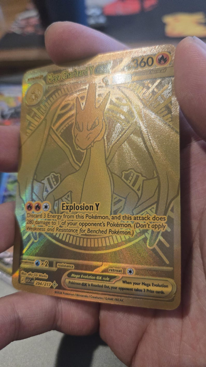 Puede incluir: Una carta coleccionable dorada que muestra a Mega Charizard Y con 360 HP. La carta presenta el texto Explosion Y, que descarta 3 Energ&iacute;as y causa 280 de da&ntilde;o. Incluye la regla Mega Evolution ex y el n&uacute;mero de serie 294/217 en la parte inferior.