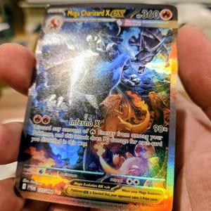 Puede incluir: Una carta coleccionable hologr&aacute;fica Mega Charizard X EX con 360 HP. La carta presenta una ilustraci&oacute;n din&aacute;mica de un drag&oacute;n con llamas azules, el texto Inferno X y reglas de juego. Muestra el n&uacute;mero de carta 125/094 y un s&iacute;mbolo de energ&iacute;a fuego.