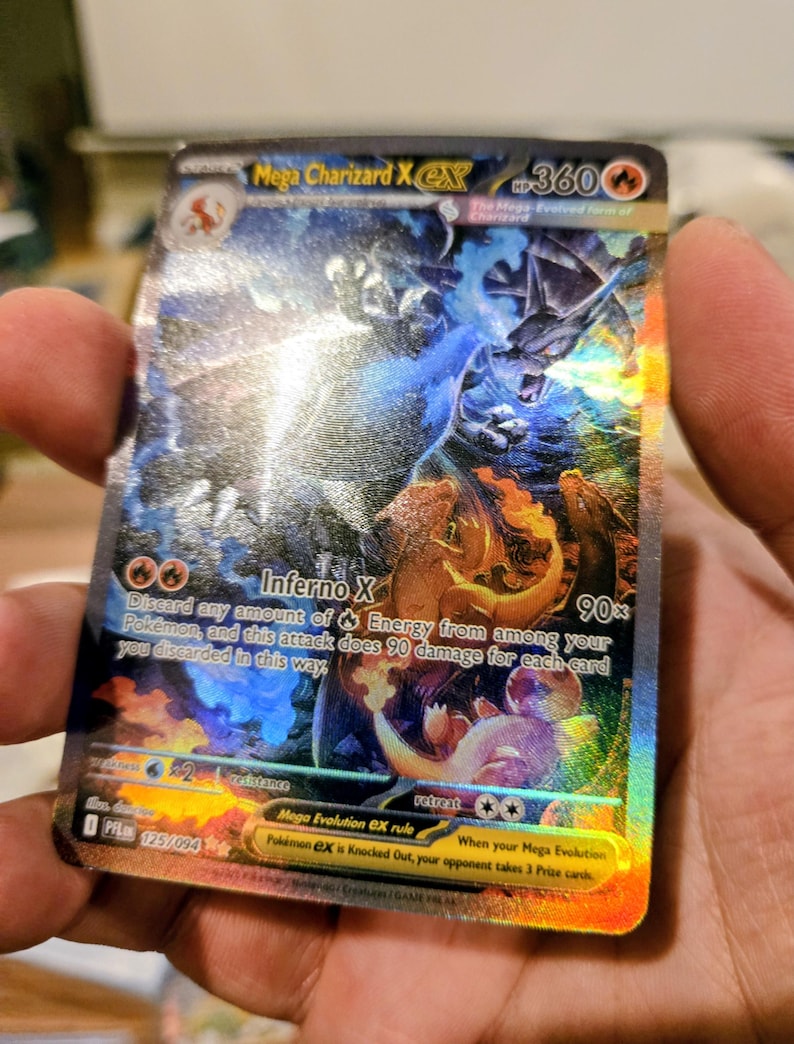 Puede incluir: Una carta coleccionable hologr&aacute;fica Mega Charizard X EX con 360 HP. La carta presenta una ilustraci&oacute;n din&aacute;mica de un drag&oacute;n con llamas azules, el texto Inferno X y reglas de juego. Muestra el n&uacute;mero de carta 125/094 y un s&iacute;mbolo de energ&iacute;a fuego.