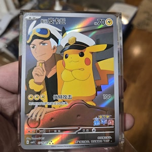 Op de afbeelding: Een holografische Pokémon-ruilkaart met Captain Pikachu en een trainer. De kaart heeft Japanse tekst, een gele Pikachu met een kapiteinshoed en een trainer met wit haar en een bril. De kaart zit in een doorzichtige beschermhoes.