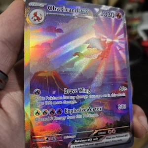 Puede incluir: Una carta coleccionable hologr&aacute;fica de Charizard ex con una vibrante ilustraci&oacute;n de un drag&oacute;n volando sobre un paisaje volc&aacute;nico. La carta muestra 330 HP, los ataques Brave Wing y Explosive Vortex, y el texto 199/165 en la esquina inferior.