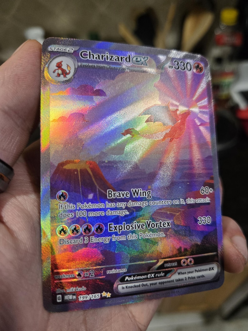 Puede incluir: Una carta coleccionable hologr&aacute;fica de Charizard ex con una vibrante ilustraci&oacute;n de un drag&oacute;n volando sobre un paisaje volc&aacute;nico. La carta muestra 330 HP, los ataques Brave Wing y Explosive Vortex, y el texto 199/165 en la esquina inferior.