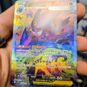 May include: A holographic Pokémon trading card featuring a purple Gengar EX character with a mischievous grin. The card has Japanese text and vibrant rainbow foil accents. The card's attack is Void Geil, with a power of 230.
