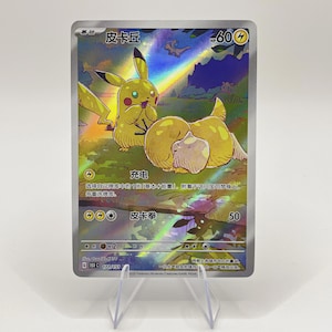Puede incluir: Una tarjeta coleccionable holográfica de Pokémon con Pikachu y una criatura amarilla. La tarjeta tiene texto japonés y un diseño de arcoíris. La tarjeta se muestra en un soporte transparente.