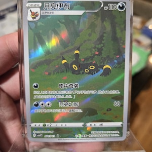 Puede incluir: Carta coleccionable Pokémon holográfica con Umbreon, un Pokémon de tipo oscuro. La carta, con texto japonés, se muestra en un soporte de plástico transparente, con un fondo de bosque.