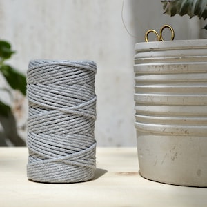 Może przedstawiać: Szpula jasnoszarej bawełnianej sznurówki, ciasno nawinięta, leży na drewnianej powierzchni. Sznurówka idealnie nadaje się do rękodzieła, makramy i innych projektów DIY.
