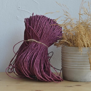 Può includere: Un grosso rotolo di spago di colore viola scuro, legato con uno spago naturale, su una superficie di legno.