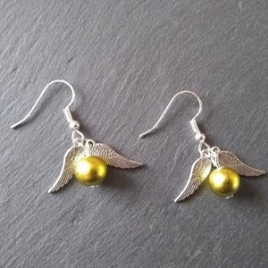 May include: A pair of silver earrings with gold-colored beads and wings. The wings are shaped like the wings of a bird.