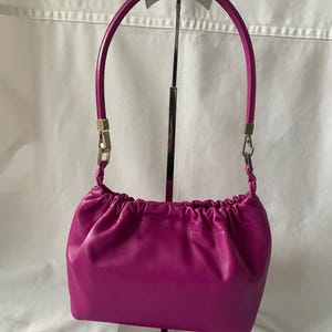 May include: A small, bright fuchsia-colored leather handbag with a gathered top and a silver metal handle.