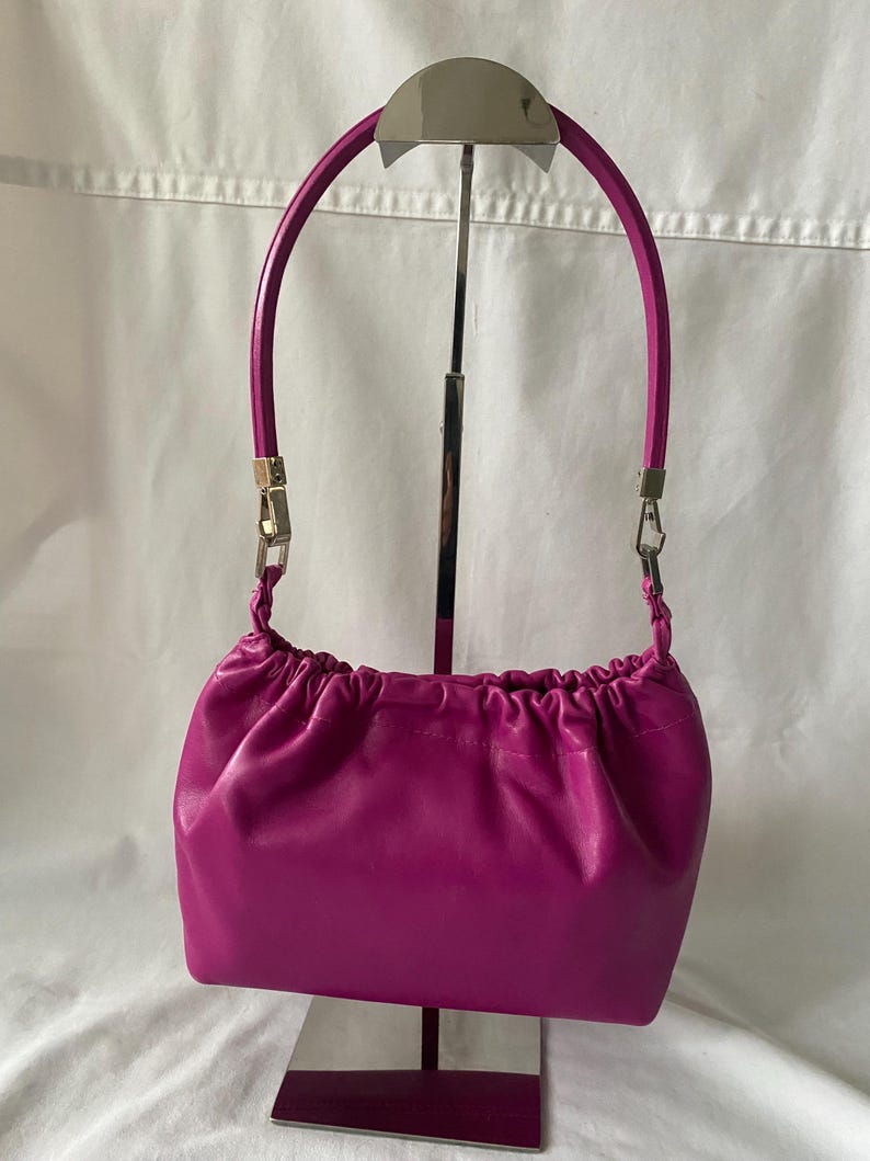 May include: A small, bright fuchsia-colored leather handbag with a gathered top and a silver metal handle.