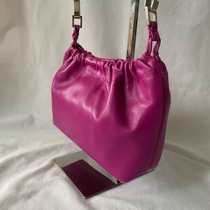 May include: A small, bright pink leather handbag with a drawstring closure and a silver chain strap.