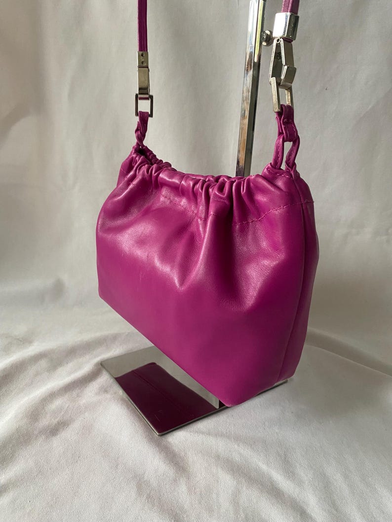 May include: A small, bright pink leather handbag with a drawstring closure and a silver chain strap.