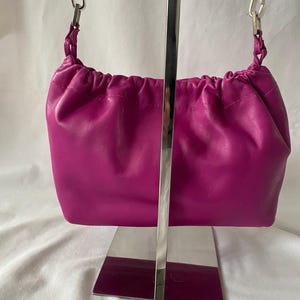 May include: A small, bright pink leather handbag with a drawstring closure and a silver chain strap.