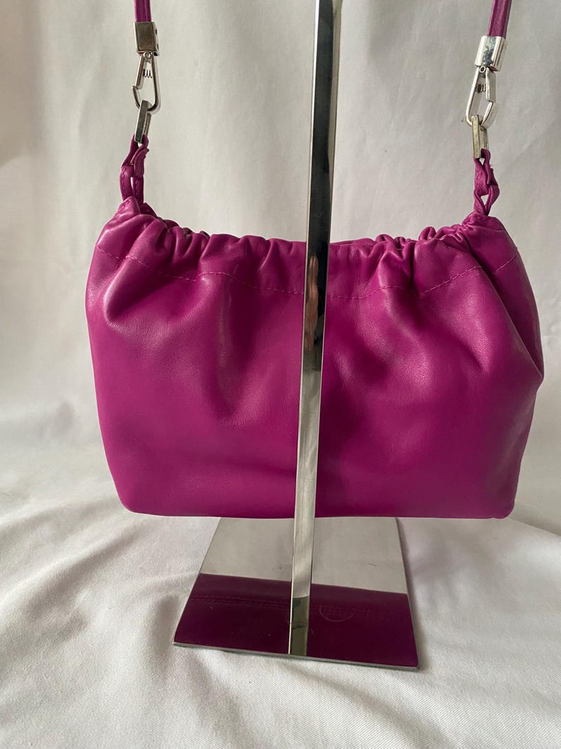 May include: A small, bright pink leather handbag with a drawstring closure and a silver chain strap.