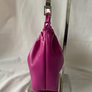 May include: A small, bright fuchsia-colored leather handbag with a silver chain strap. The bag is on a display stand.
