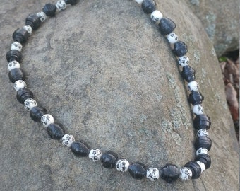 May include: Black and white patterned beads strung on a necklace. The beads are made of paper and have a floral design.
