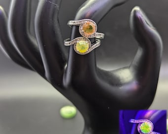 May include: A silver ring with two round, iridescent stones. The stones are yellow-green in regular light and glow green under a blacklight.