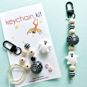 May include: A keychain kit with a black clasp, wooden beads, black and white striped beads, and a black bead with a white spiderweb design. The kit includes white ghost-shaped beads and a card that says "keychain kit".