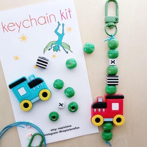 May include: A keychain kit with a blue and red train charm, green beads, and black and white patterned beads. The kit includes a green string and a silver clasp. The card reads "keychain kit" and includes the Etsy and Instagram handles for the seller.