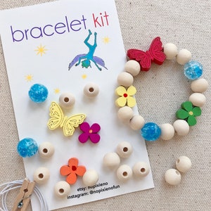 May include: A bracelet kit with wooden beads, colorful butterfly and flower charms, and blue glitter beads. The kit includes instructions and a string for making a bracelet. The card reads "bracelet kit" and includes social media handles for the seller.