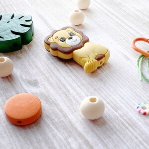 May include: A set of wooden and silicone baby teethers, including a lion, a leaf, a round orange teether, and a few wooden beads. The teethers are strung on a green cord with a plastic clip.
