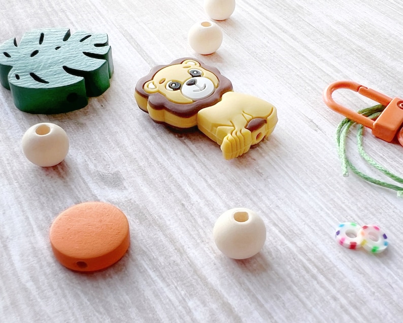 May include: A set of wooden and silicone baby teethers, including a lion, a leaf, a round orange teether, and a few wooden beads. The teethers are strung on a green cord with a plastic clip.